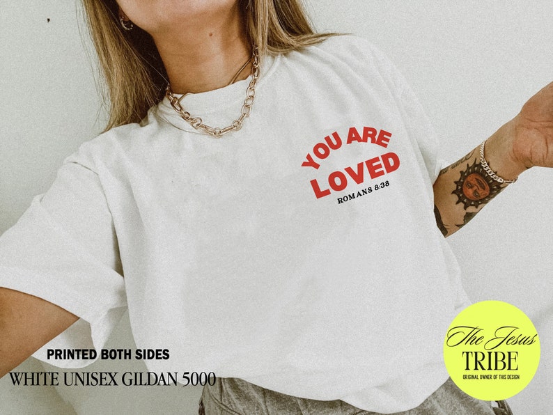 K&ouml;nnte beinhalten: Wei&szlig;es Unisex-T-Shirt mit dem Text "YOU ARE LOVED" in roten Buchstaben und dem Text "ROMANS 8:38" in schwarzen Buchstaben. Das Shirt ist beidseitig bedruckt.