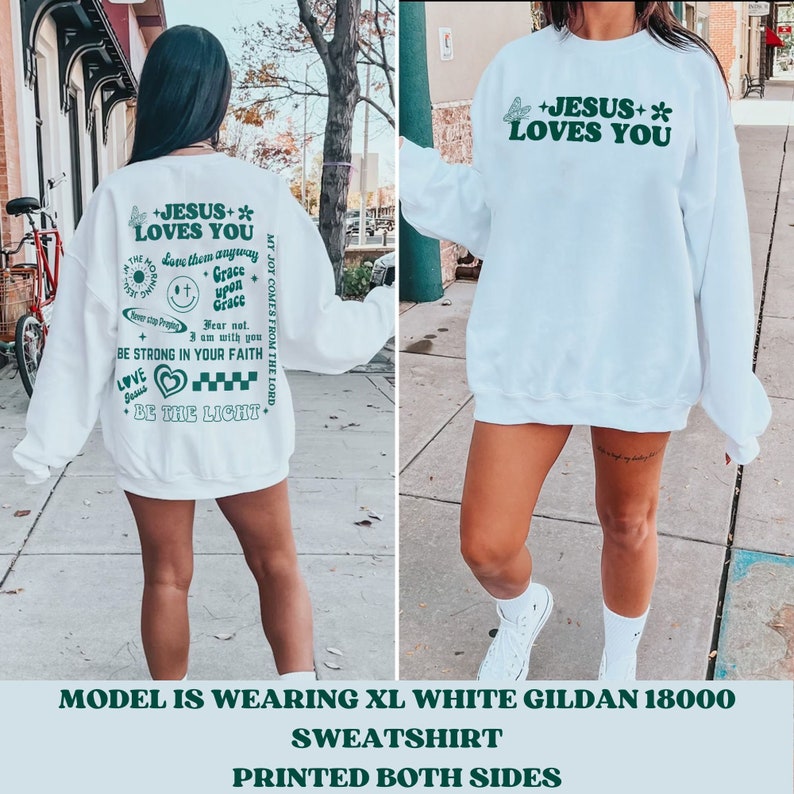 May include: White sweatshirt with the text "+JESUS+ LOVES YOU" in green, along with other phrases and graphics. The back of the sweatshirt has additional text and graphics in green. The sweatshirt is a Gildan 18000.