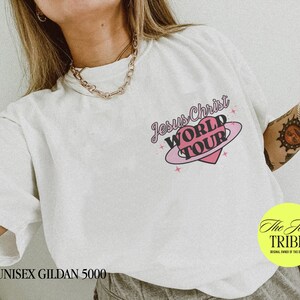 Puede incluir: Camiseta blanca unisex Gildan 5000 con un gr&aacute;fico de coraz&oacute;n rosa y el texto "Jesus Christ World Tour".