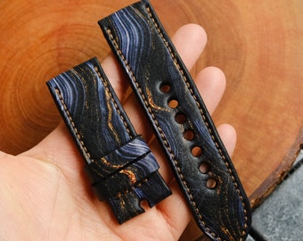 Könnte beinhalten: Zwei schwarze Lederarmbänder mit einem blauen und goldenen Marmormuster und braunen Nähten.