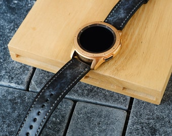 Peut inclure: Une montre connectée en or rose avec un bracelet en cuir noir. Le cadran de la montre est rond et possède un écran noir.