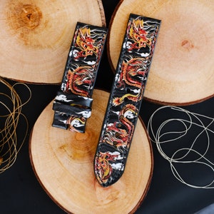 Pode incluir: Duas pulseiras de relógio de couro preto com um design de dragão. As pulseiras têm um fundo branco com dragões vermelhos, laranja e amarelos.