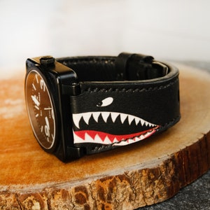 May include: Black leather watch strap with a white and red shark tooth design.