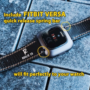 Puede incluir: Correa de reloj de cuero negro con costuras marrones y el texto "12 RUSLIE CO" en la correa. La correa est&aacute; unida a un reloj inteligente Fitbit Versa plateado.