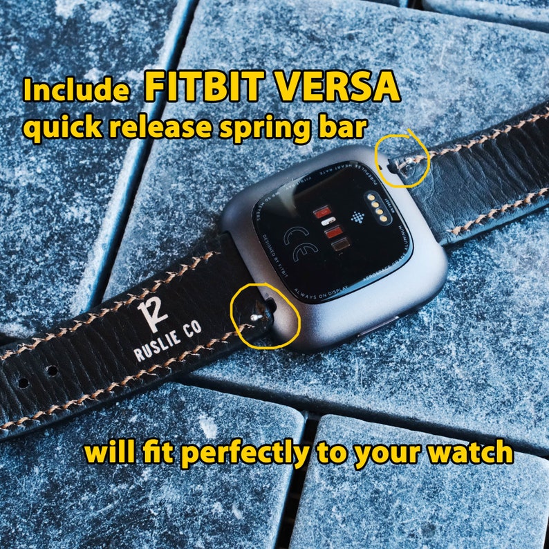 Puede incluir: Correa de reloj de cuero negro con costuras marrones y el texto "12 RUSLIE CO" en la correa. La correa est&aacute; unida a un reloj inteligente Fitbit Versa plateado.