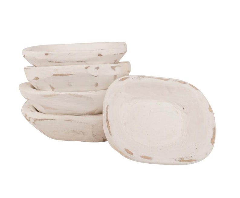 Op de afbeelding: Een stapel van vier kleine, ovale houten kommen met een verweerde witte verfafwerking, vergezeld door een bijpassende kom die ervoor is geplaatst. Elke kom heeft zichtbare houtnerven en versleten randen die het natuurlijke bruine hout tonen.