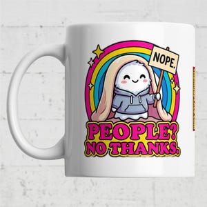 Op de afbeelding: Witte keramische mok met een cartoonfiguur met een bordje met de tekst "NOPE". Het figuur staat tegen een regenboog- en sterrenontwerp, met de tekst "PEOPLE? NO THANKS." eronder. De mok heeft een wit handvat.