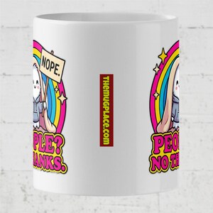 Op de afbeelding: Witte keramische mok met een cartoon konijn met een bord met de tekst "NOPE". Het konijn staat tegen een regenboog en sterren design. De mok heeft ook de tekst "PEOPLE? THANKS" en "PEOPLE? NOTH".