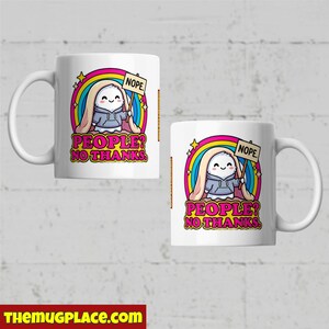 Op de afbeelding: Twee witte keramische mokken met een cartoonafbeelding. De afbeelding toont een lachend personage met een "NOPE"-bord, tegen een regenboog en de tekst "PEOPLE? NO THANKS." De mokken hebben een gebogen handvat.