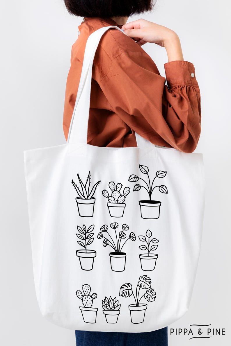 May include: White canvas tote bag featuring black line drawings of potted plants. The bag has the text "PIPPA & PINE" printed on the bottom.