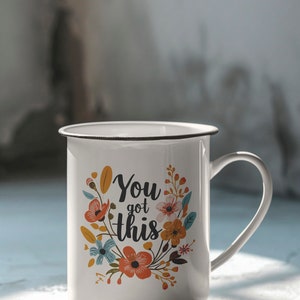 May include: White enamel mug with a black rim and handle. The mug has a floral design and the text "You got this" in black.
