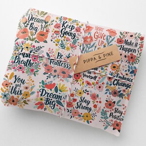 May include: A pink and white gift wrap with a floral pattern and inspirational quotes like "Dream Big", "Keep Going", "Be Fearless", and "Never Give Up". The gift wrap is tied with a string and has a brown tag that says "Pippa & Pine".