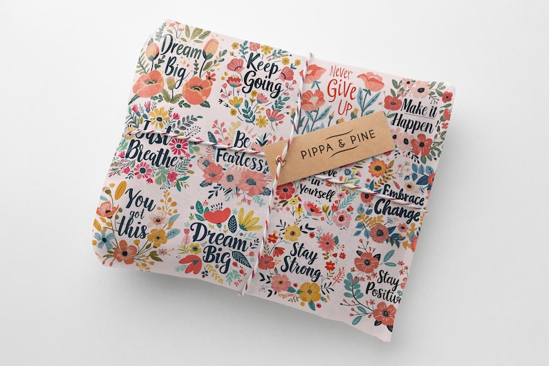 May include: A pink and white gift wrap with a floral pattern and inspirational quotes like "Dream Big", "Keep Going", "Be Fearless", and "Never Give Up". The gift wrap is tied with a string and has a brown tag that says "Pippa & Pine".
