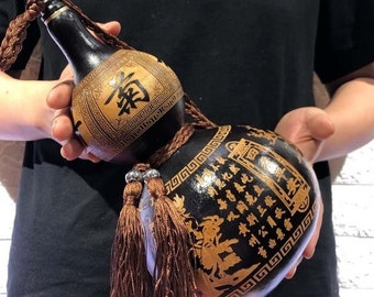 May include: A black and gold gourd bottle with intricate carvings and Chinese characters. The bottle has a brown tassel and is decorated with a geometric pattern.