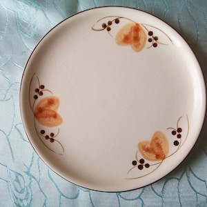 Puede incluir: Un plato de cerámica blanco con un borde marrón y un diseño floral sencillo en tonos marrones y naranjas.
