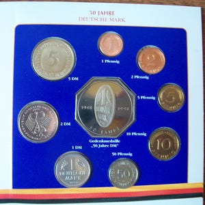 Könnte beinhalten: Ein blaues und goldenes Münzsammel-Display mit verschiedenen deutschen Münzen, darunter 1, 2, 5 und 10 Pfennig, 1 und 2 Deutsche Mark sowie eine Gedenkmünze 50 Jahre Deutsche Mark. Das Display enthält auch den Text "50 Jahre Deutsche Mark" und "Gedenkmedaille 50 Jahre DM".