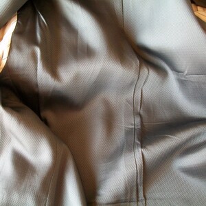 May include: Close-up of the inside of a gray suit jacket. The fabric is textured and has a subtle sheen.