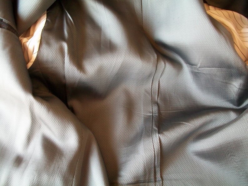 May include: Close-up of the inside of a gray suit jacket. The fabric is textured and has a subtle sheen.