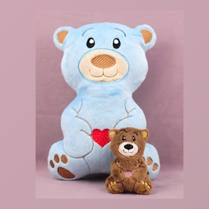 May include: Two plush teddy bears, one light blue and one brown, are sitting side-by-side. The blue bear is larger and has a red heart embroidered on its chest. The brown bear is smaller and has a simple embroidered face.