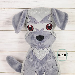 May include: Grey plush dog toy with embroidered details, including red eyes and a black nose. The toy is sitting on a white wooden surface. 6x10