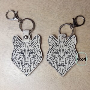 May include: Two white keychains with black geometric wolf designs. The keychains are attached to silver key rings.