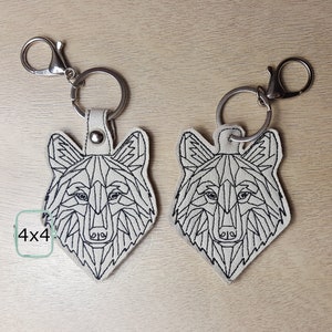 May include: Two white felt keychains with black geometric wolf designs. Each keychain has a silver metal ring and a silver metal clasp.