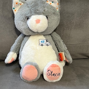 May include: Gray and white plush cat toy with a mail truck design on the chest and the name "Stacie" embroidered on one foot.