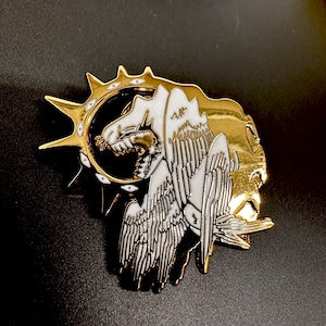 May include: Gold and white enamel pin featuring a stylised angel with wings outstretched, surrounded by a sunburst with eyes.