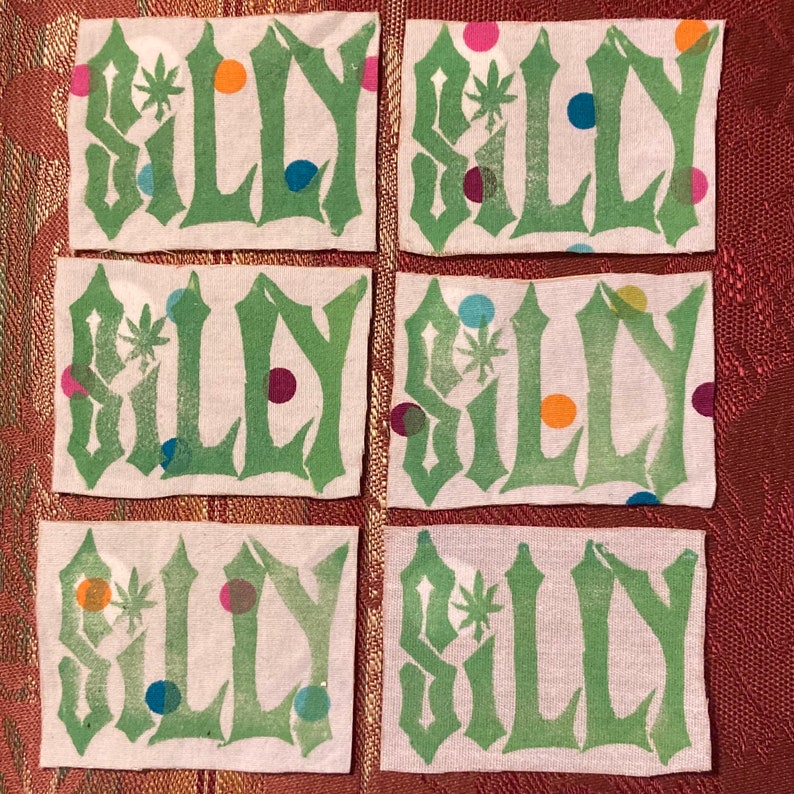 May include: Six white fabric patches with the word "SILLY" printed in green letters. Each patch has a different arrangement of colorful dots.