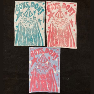 May include: Three fabric patches with the text "Boys Don't Cry" in a colorful, stylized font. Each patch features a cartoon clown with a teardrop on its cheek. The patches are in blue, pink, and light blue.