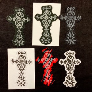 May include: Five iron-on patches featuring a stylized cross design with a skull in the center. The crosses are in black, white, and red.