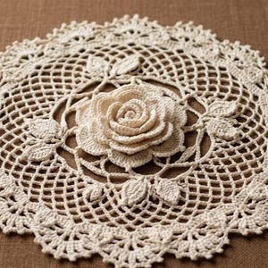 Può includere: Un centrino rotondo all'uncinetto color bianco sporco con un intricato motivo a reticolo traforato. Il centro è decorato con un motivo a rosa tridimensionale a più strati, circondato da piccole foglie all'uncinetto e un bordo decorativo smerlato.