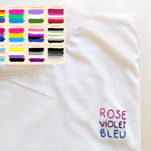 Peut inclure: T-shirt blanc avec les mots "ROSE", "VIOLET" et "BLEU" brodés en fil rose, violet et bleu.