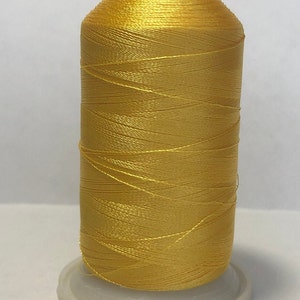 Puede incluir: Una bobina de hilo amarillo brillante, bien enrollada, con una parte superior roja y blanca. El hilo est&aacute; sobre una base de pl&aacute;stico blanco, adecuado para proyectos de costura y manualidades.