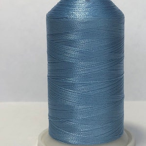 Puede incluir: Una bobina de hilo azul claro con una tapa roja. El hilo est&aacute; enrollado sobre una base de pl&aacute;stico blanco. El hilo tiene un ligero brillo, lo que sugiere un material sint&eacute;tico. Ideal para proyectos de costura y bordado. La bobina mide unos 10 cm de alto.