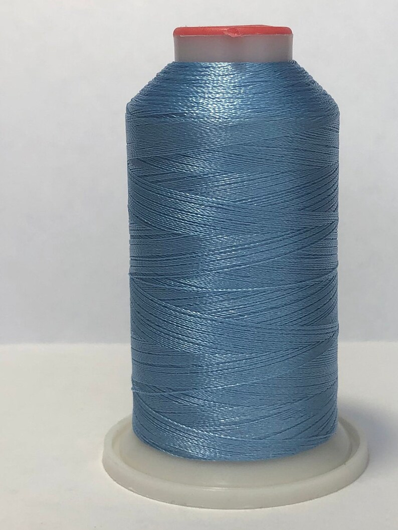 Puede incluir: Una bobina de hilo azul claro con una tapa roja. El hilo est&aacute; enrollado sobre una base de pl&aacute;stico blanco. El hilo tiene un ligero brillo, lo que sugiere un material sint&eacute;tico. Ideal para proyectos de costura y bordado. La bobina mide unos 10 cm de alto.