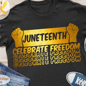 May include: A black t-shirt with a gold graphic design that says "Juneteenth Celebrate Freedom". The graphic design features a raised fist and the text is repeated multiple times in a layered effect.