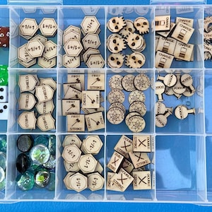 May include: A clear plastic storage box with multiple compartments containing various wooden game pieces. The pieces are in different shapes and sizes, and some have text on them, such as "+1/+1", "First Strike", and "Hexproof".