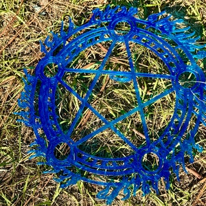 May include: A blue pentagram with a circle around it, with a design of runes and symbols. The pentagram is on a background of green grass.