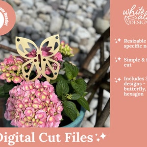 May include: A gold butterfly-shaped metal plant stake, shown in a pot of pink flowers. The image includes the text "Glowforge Laser Ready!" and "white alder DESIGNS". The text "Digital Cut Files" is also included in the image.