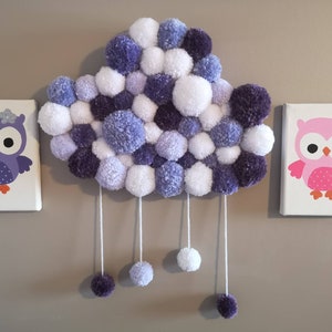 May include: A purple and white pom-pom cloud mobile with two owl canvases, one purple and one pink, hanging on a wall.