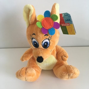 May include: A plush brown kangaroo toy with a yellow belly, blue eyes, and a colorful flower on its head. The toy has a "Waliibi" tag attached to it.