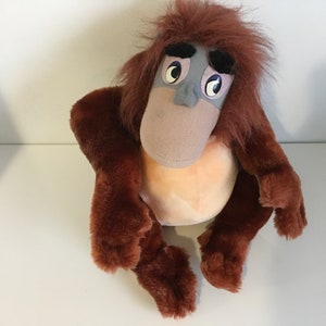 May include: A brown plush orangutan with a gray face and large eyes. The orangutan is sitting with its legs crossed.