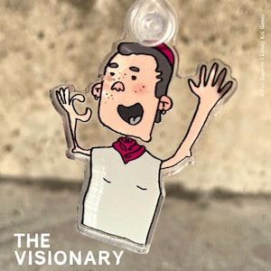 Könnte beinhalten: Eine Comicfigur mit einem roten Bandana und einem weißen Tanktop, mit dem Text "THE VISIONARY" darunter. Die Figur lächelt und hat eine rosa Nase und rote Wangen. Die Figur ist aus klarem Acryl.