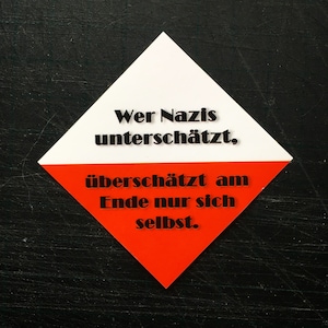 May include: A white and red diamond-shaped sticker with black text. The text reads, "Wer Nazis unterschätzt, überschätzt am Ende nur sich selbst."