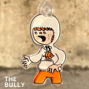 Könnte beinhalten: Ein weißer Plastik-Schlüsselanhänger mit einer Cartoon-Illustration eines Jungen, der ein weißes Hoodie mit einem orangefarbenen Basketball und dem Text "League" trägt. Der Junge trägt eine orangefarbene Hose und hat rote Haare. Der Schlüsselanhänger ist mit "THE BULLY" beschriftet.