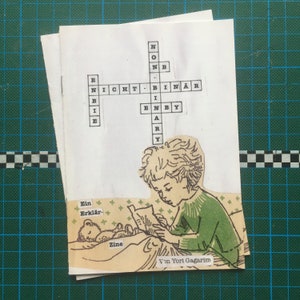 Könnte beinhalten: Ein Kreuzworträtsel mit den Wörtern "NICHT" und "BINÄR" in der Mitte. Das Rätsel ist auf weißem Hintergrund mit einer Zeichnung eines Kindes, das ein Buch liest. Der Text "Von Yori Gagarim" befindet sich am unteren Rand des Bildes.