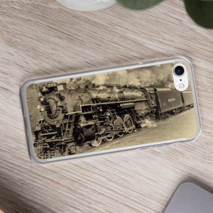 Può includere: Una fotografia vintage in bianco e nero di una locomotiva a vapore con fumo che esce dal camino. Il treno è su un binario e sta procedendo in avanti. L'immagine è su una custodia per telefono trasparente.