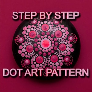 Pode incluir: Padrão de arte de pontos passo a passo em uma rocha preta. O padrão apresenta pontos rosa e vermelhos dispostos em um design de mandala.