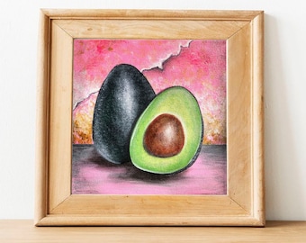 May include: A framed painting of two avocados, one whole and one sliced open, on a pink background. The avocado halves are painted in a realistic style with green skin and a brown pit.
